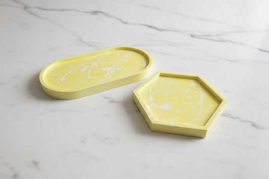 Two yellow trays, one oval and one hexagonal, on a marble surface.